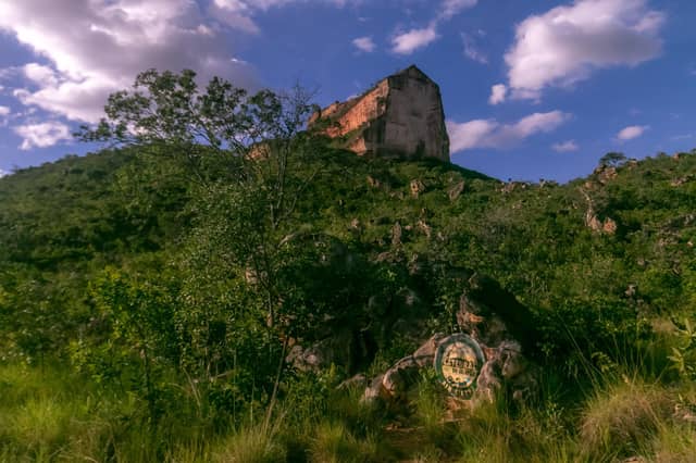 The towering sandstone rock formation of Catedral do Jalapão rising above a green cerrado hillside, with a circular site marker sign visible among the boulders at the trailhead — a landmark reached on brazil 4x4 tours through Tocantins