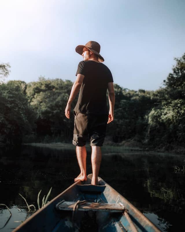 A traveler standing on the bow of a wooden canoe at sunrise during an Amazon canoe trip on calm blackwater