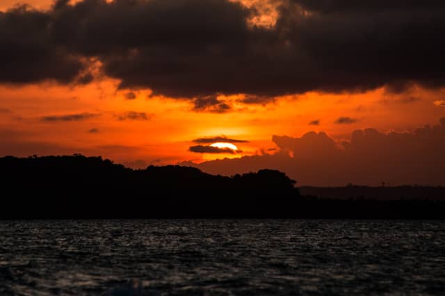 Fiery orange and red sunset over the silhouetted Atlantic Forest coastline of Itacaré, reflected across dark choppy water