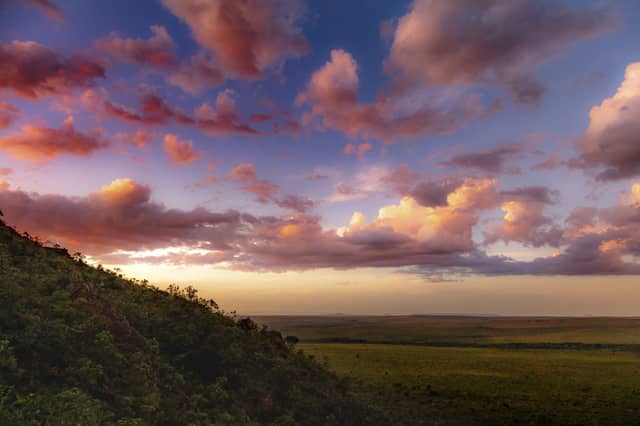 Panoramic sunset view over the flat Cerrado savanna of Jalapão, with pink and golden clouds filling a wide sky above a forested hillside in Tocantins, Brazil