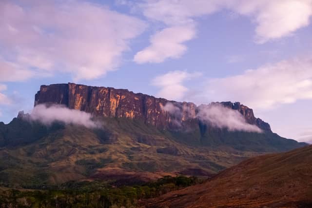 Mount Roraima's sheer sandstone cliffs glowing amber at sunset, wrapped in low clouds above the Gran Sabana highlands on a mount roraima tour