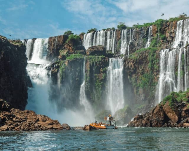 Boat tour approaching the base of Iguazu Falls under a blue sky