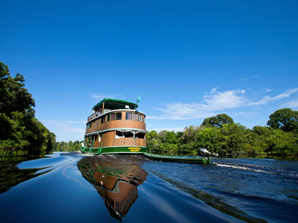 A multi-level traditional wooden river cruise boat navigates the reflective dark waters of the Amazon.