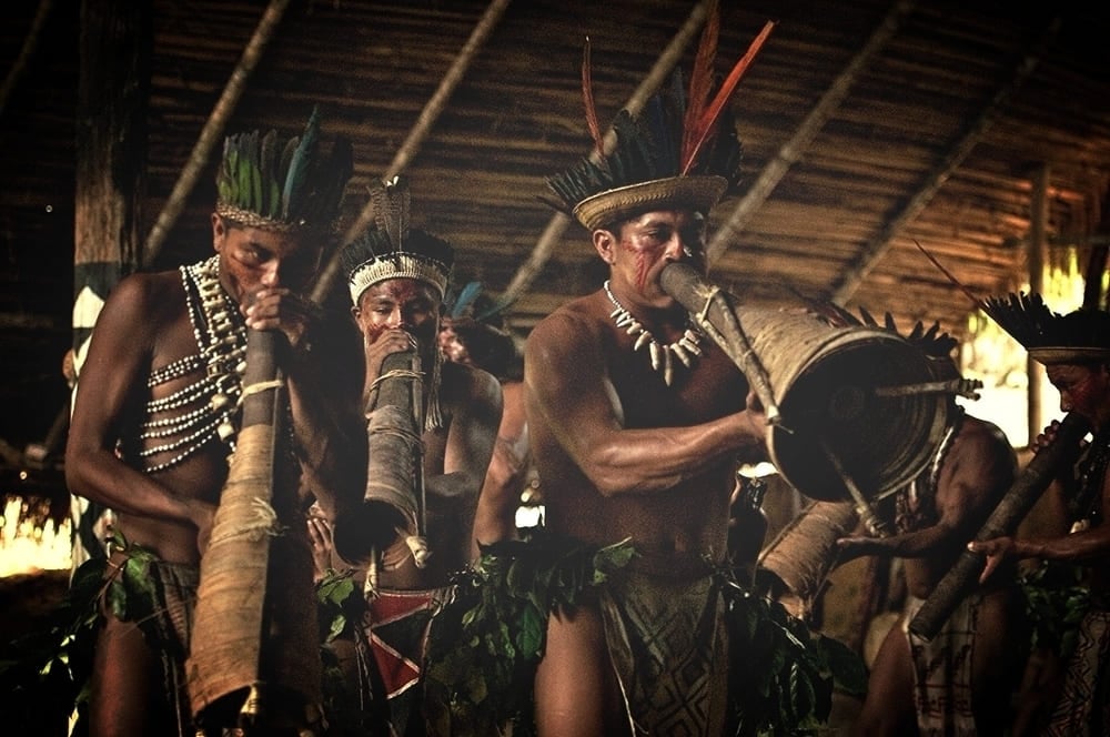 A group of indigenous people in the Amazon playing traditional long wind instruments and drums during a cultural ritual.