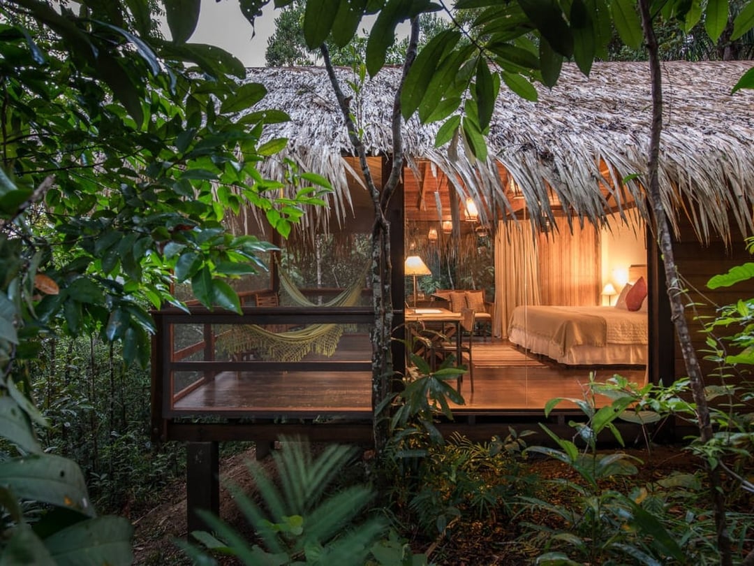 Amazon jungle lodge bungalow on stilts with a hammock and lit bedroom surrounded by rainforest