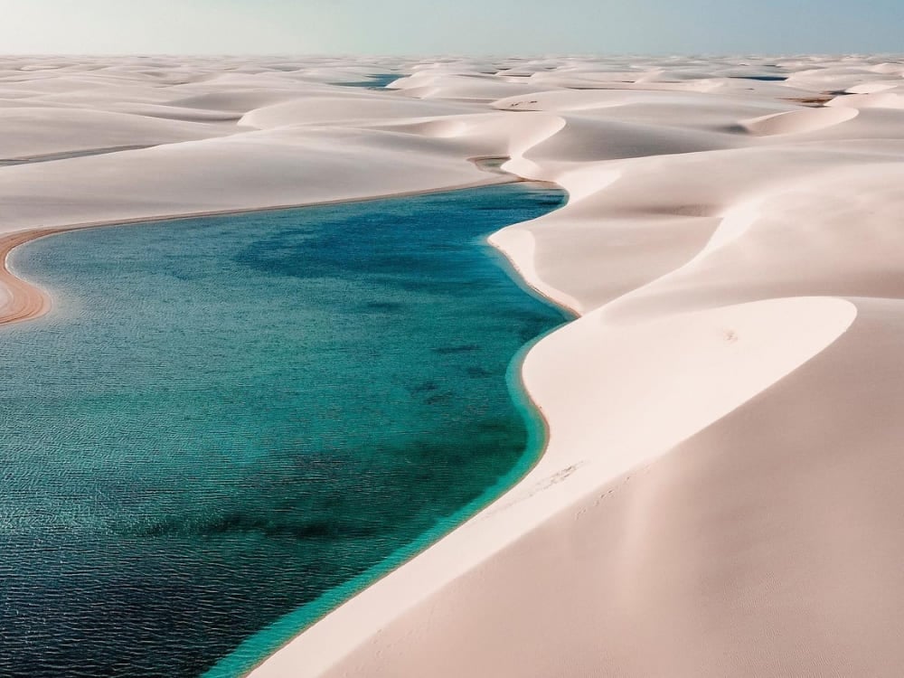 Aerial view of a long turquoise lagoon winding between the white sand dunes of Lençóis Maranhenses.