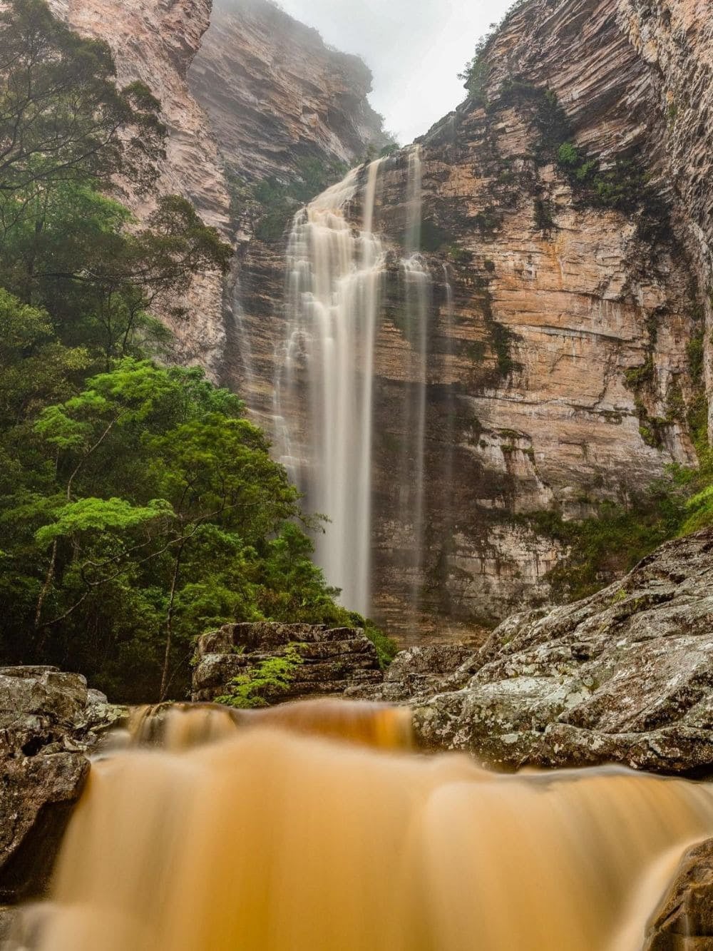 The Cachoeira da Encantada dropping down a canyon wall above an orange river in Chapada Diamantina, Brazil.