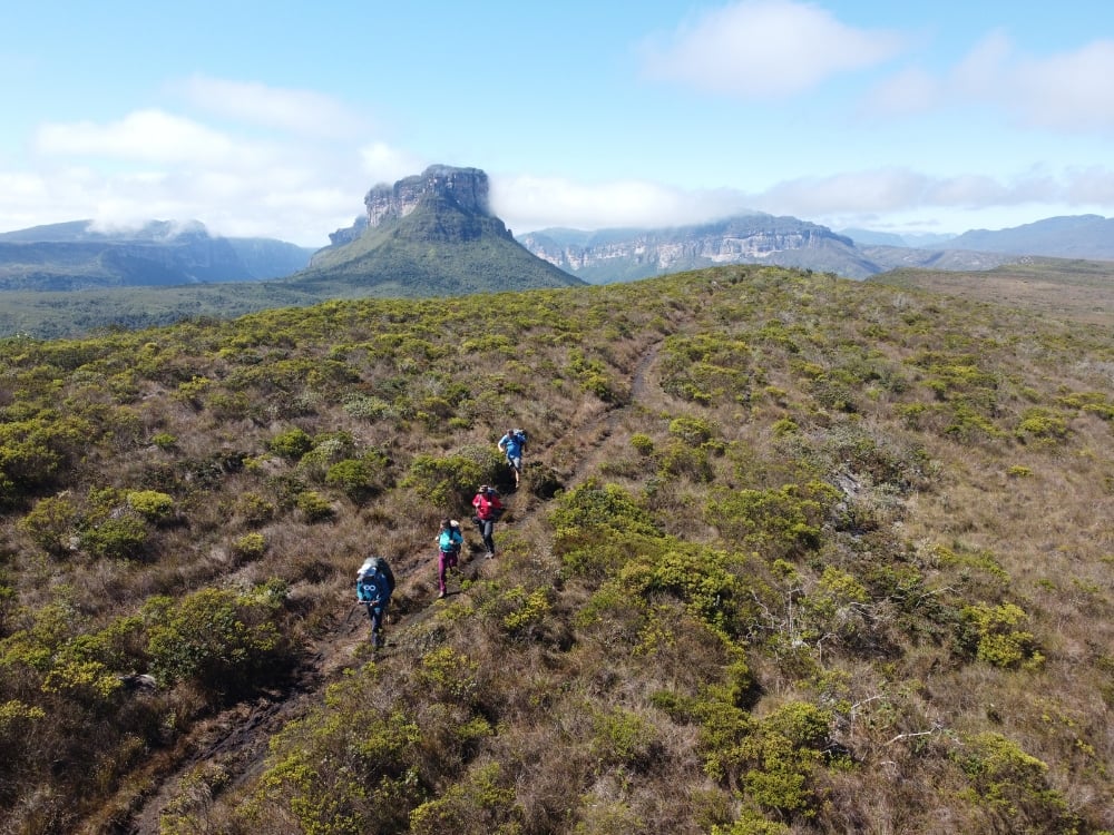 Aerial view of hikers crossing a plateau trail toward a flat-topped mountain in Chapada Diamantina, Brazil.