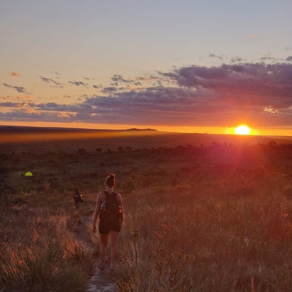 A hiker walking a plateau trail at sunset beside a tent in Chapada Diamantina, Brazil.