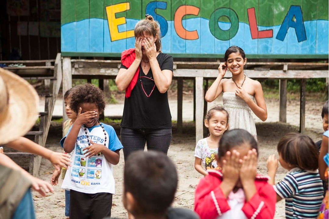 Group of smiling local children and a tourist interacting in front of a riverside community school building in the Amazon. Group of smiling local children and a tourist interacting in front of a riverside community school building in the Amazon.