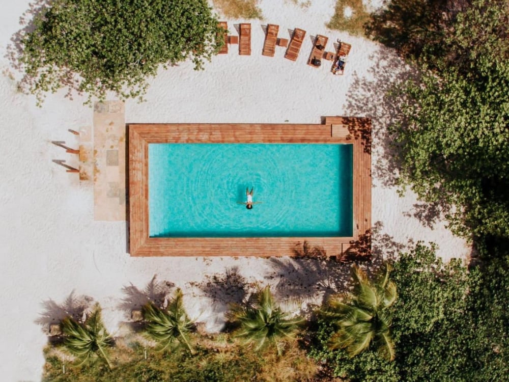 Vertical aerial shot of a rectangular turquoise swimming pool with a smooth wooden deck and loungers at the luxurious La Ferme De Georges. Vertical aerial shot of a rectangular turquoise swimming pool with a smooth wooden deck and loungers at the luxurious La Ferme De Georges.