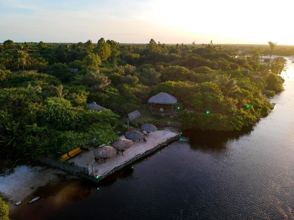 Aerial view of the camp-style Ciamat Camp, highlighting thatched kiosks and a deck by the water surrounded by vegetation. Aerial view of the camp-style Ciamat Camp, highlighting thatched kiosks and a deck by the water surrounded by vegetation.