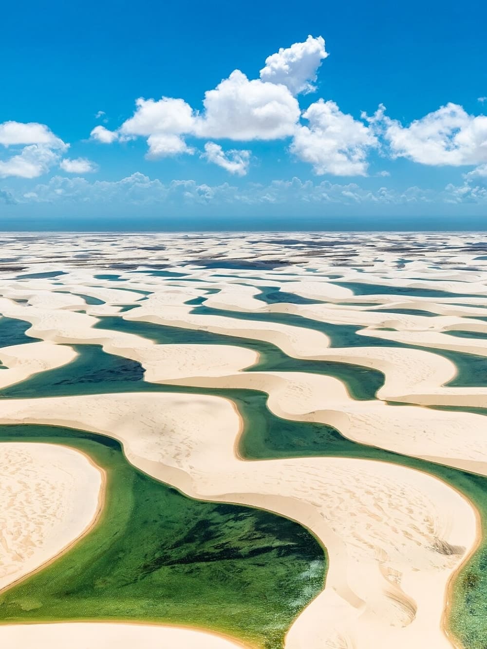Aerial view of white sand dunes and freshwater lagoons stretching across the Lencois Maranhenses landscape under a blue sky. Aerial view of white sand dunes and freshwater lagoons stretching across the Lencois Maranhenses landscape under a blue sky.