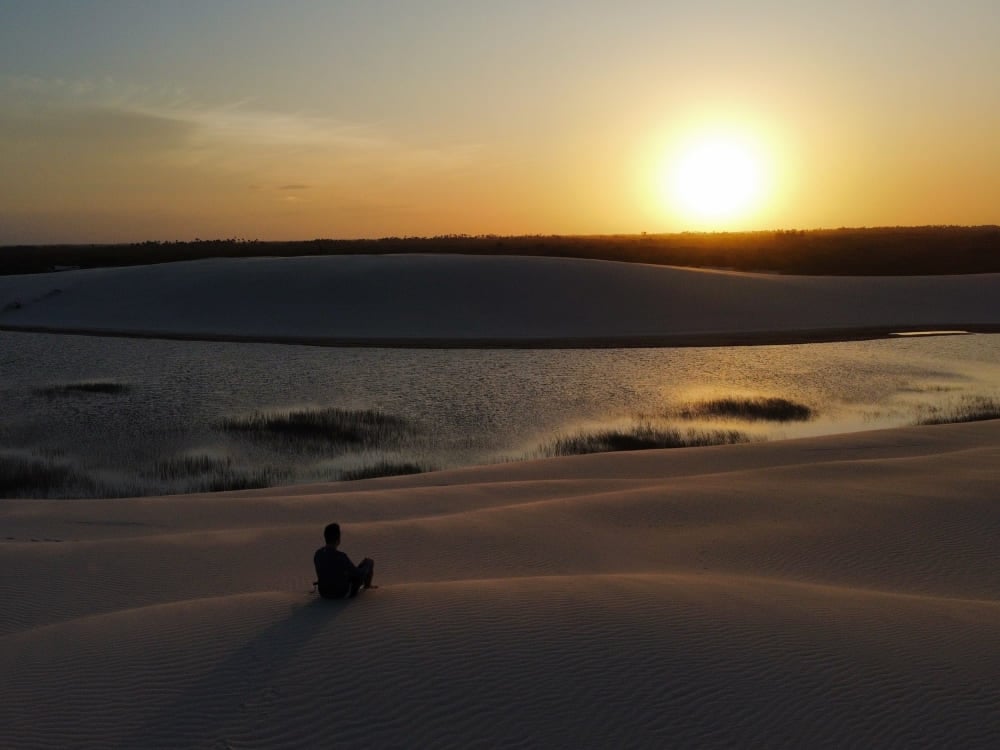 Silhouette of a person sitting on a sand dune, watching a golden sunset over the lagoons of Lençóis Maranhenses. Silhouette of a person sitting on a sand dune, watching a golden sunset over the lagoons of Lençóis Maranhenses.