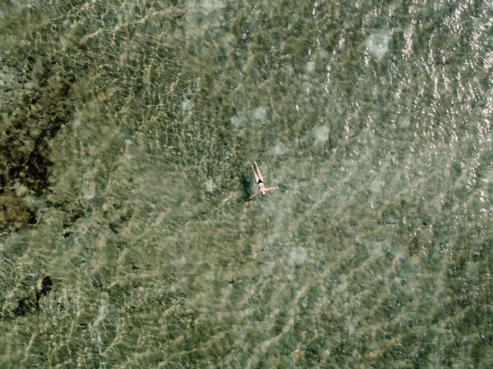 Top-down view of a person swimming in a crystal-clear rainwater lagoon in Lençóis Maranhenses, revealing the sandy bottom. Top-down view of a person swimming in a crystal-clear rainwater lagoon in Lençóis Maranhenses, revealing the sandy bottom.
