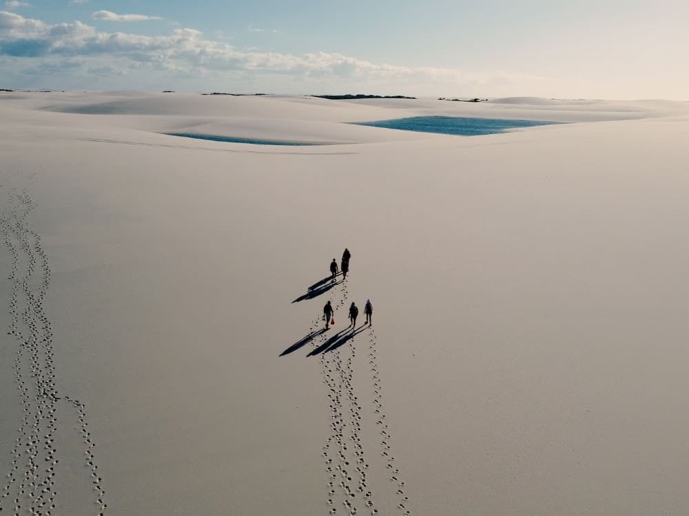 Aerial view of a group trekking across the immense white sand dunes of Lençóis Maranhenses, with small blue lagoons in the background. Aerial view of a group trekking across the immense white sand dunes of Lençóis Maranhenses, with small blue lagoons in the background.
