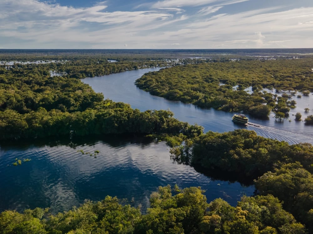 Aerial view of a riverboat navigating the Jaú River basin surrounded by the vast green Amazon Rainforest. Aerial view of a riverboat navigating the Jaú River basin surrounded by the vast green Amazon Rainforest.
