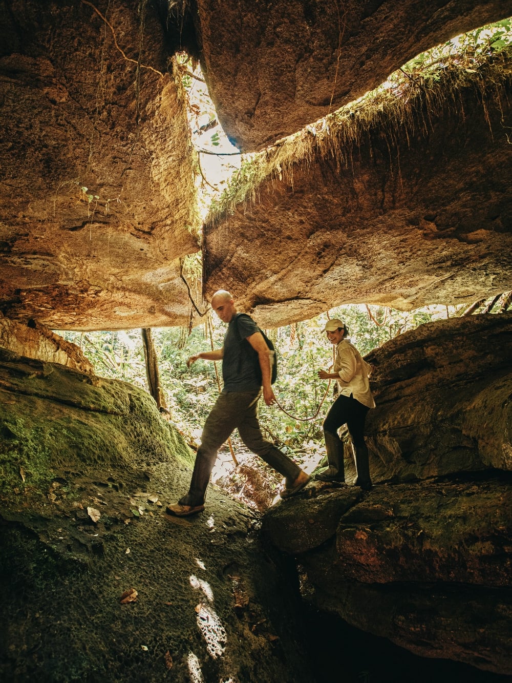 Two travelers hiking under a massive rock formation in the Presidente Figueiredo forest. Two travelers hiking under a massive rock formation in the Presidente Figueiredo forest.