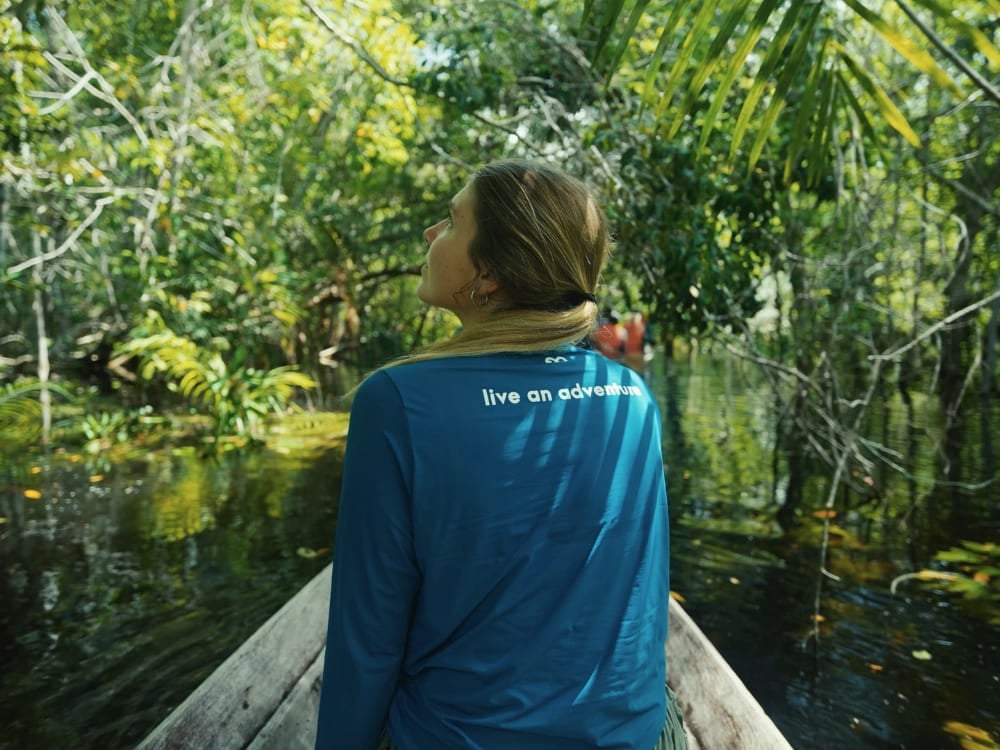 . Tourist navigating a canoe through the green canopy of the flooded Amazon rainforest looking up at the trees.