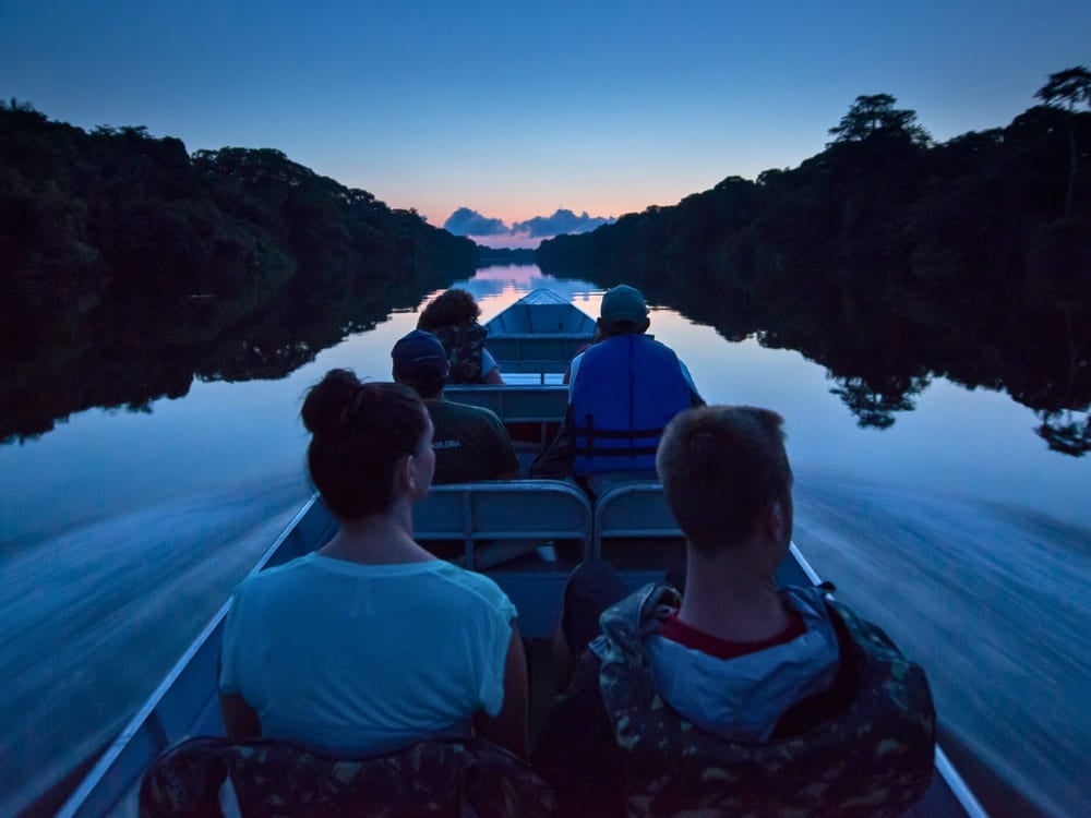 Tourists on a small motorized canoe navigating an Amazon river at twilight.