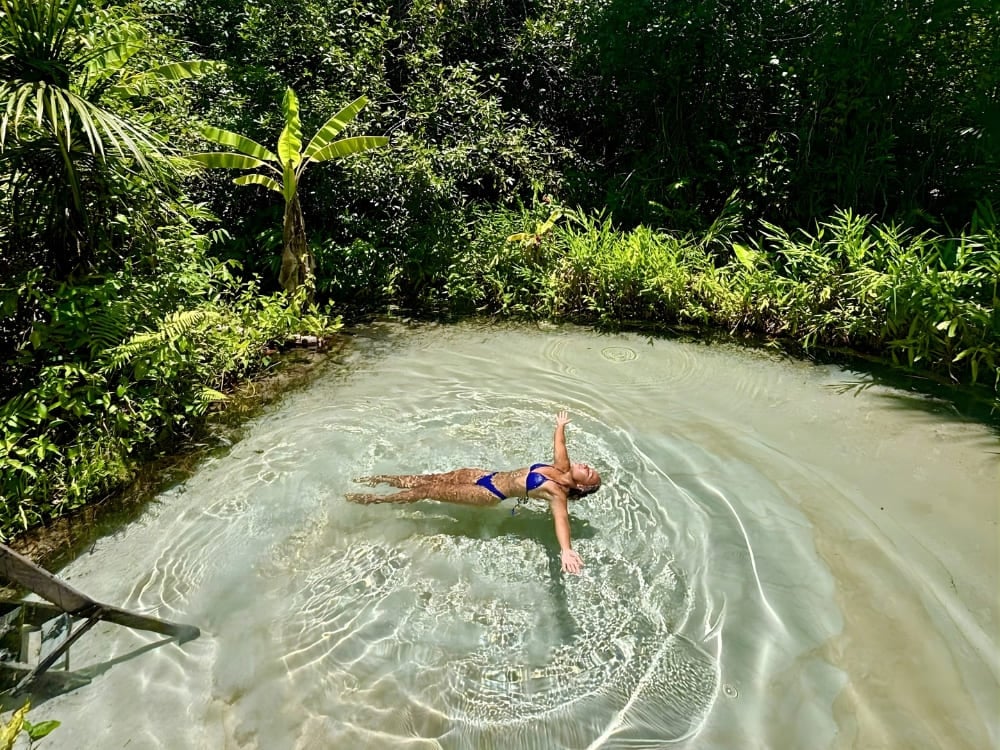 Woman floating on her back with her arms spread in crystal clear light blue waters, surrounded by tropical trees and dense green vegetation. Woman floating on her back with her arms spread in crystal clear light blue waters, surrounded by tropical trees and dense green vegetation.