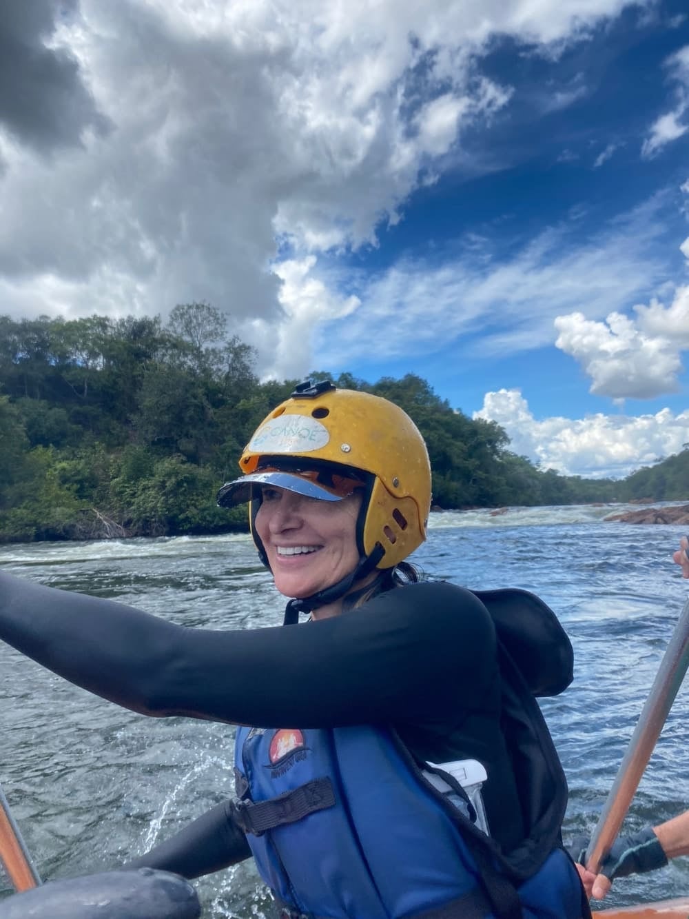 Woman with her arms raised in celebration on the summit of a dark rocky cliff, standing out above a dense sea of white clouds. Mulher madura fazendo rafting no Jalapão