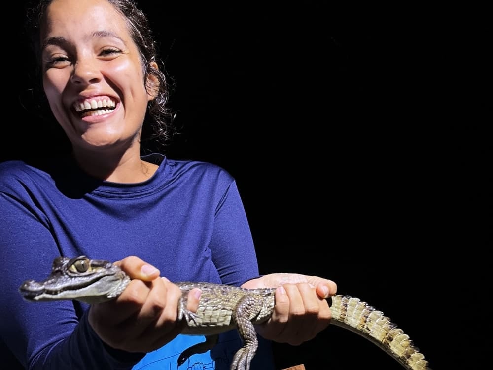 Mariana smiles enthusiastically while safely holding a small alligator during a night excursion in the Amazon. Mariana smiles enthusiastically while safely holding a small alligator during a night excursion in the Amazon.