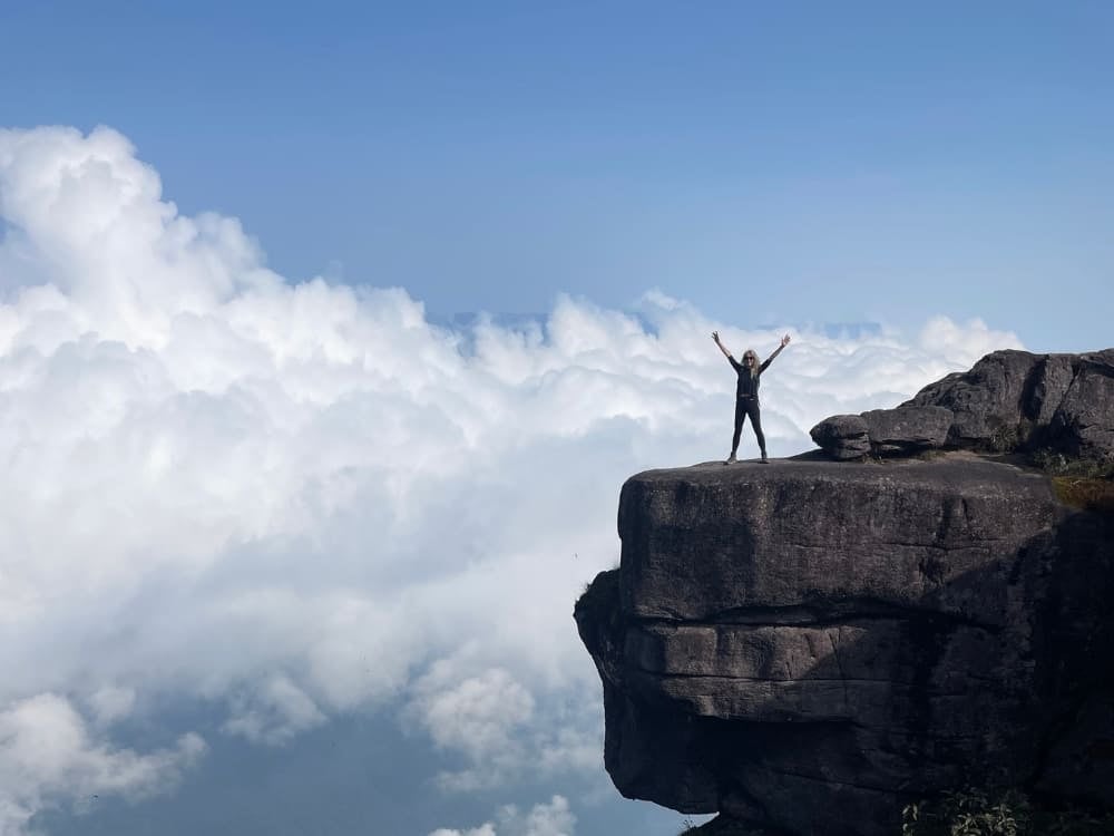 Silhouette of a woman with her arms raised in a sign of victory on the edge of the rocky cliff of Mount Roraima, above the white clouds. Silhouette of a woman with her arms raised in a sign of victory on the edge of the rocky cliff of Mount Roraima, above the white clouds.