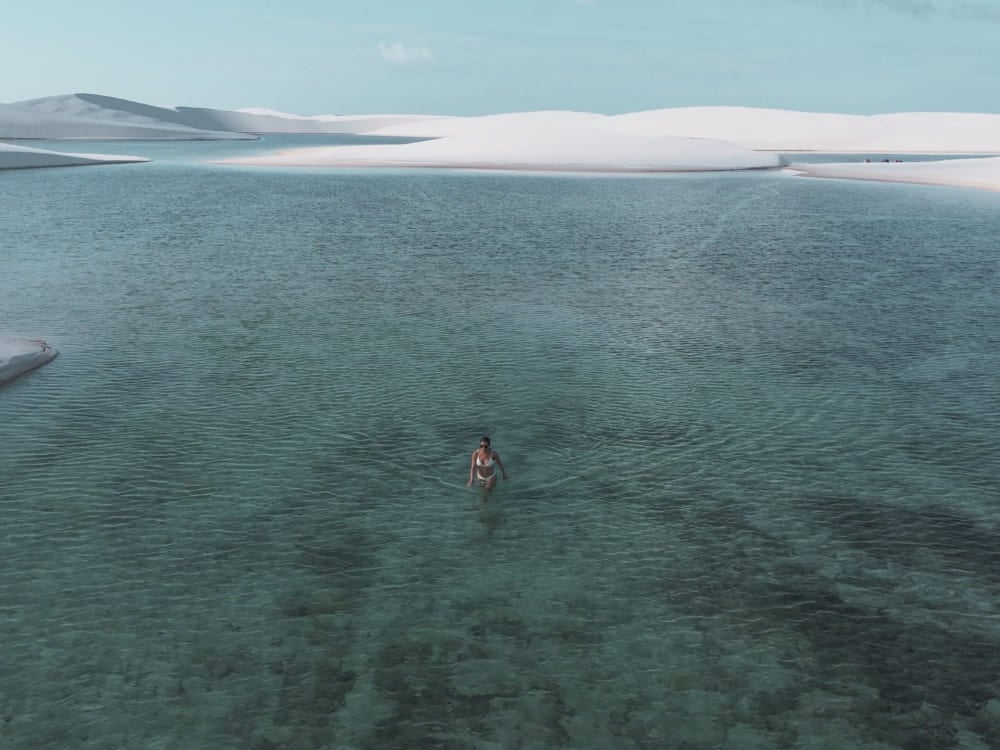 Woman walking in the shallow, crystal-clear waters of a lagoon surrounded by the large white sand dunes of Lençóis Maranhenses. Woman walking in the shallow, crystal-clear waters of a lagoon surrounded by the large white sand dunes of Lençóis Maranhenses.