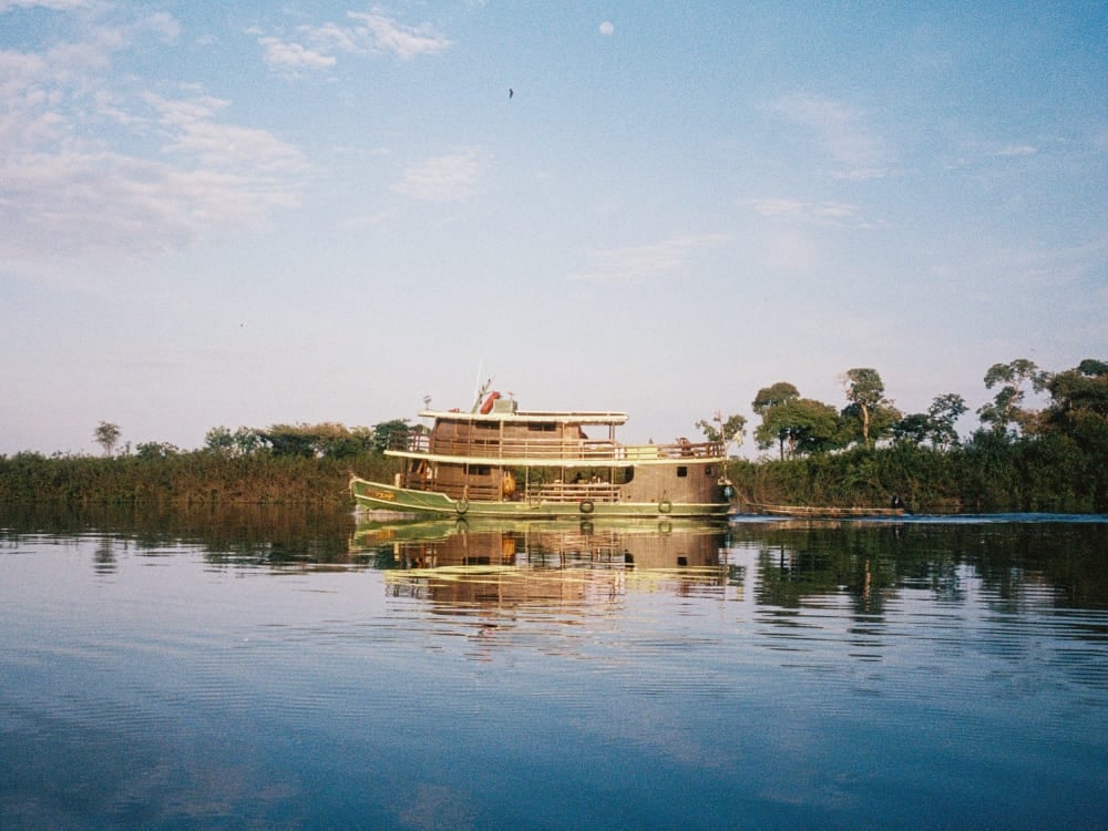 Traditional river cruise boat navigating the calm waters of the Rio Negro, with green vegetation reflecting on the water. Traditional river cruise boat navigating the calm waters of the Rio Negro, with green vegetation reflecting on the water.