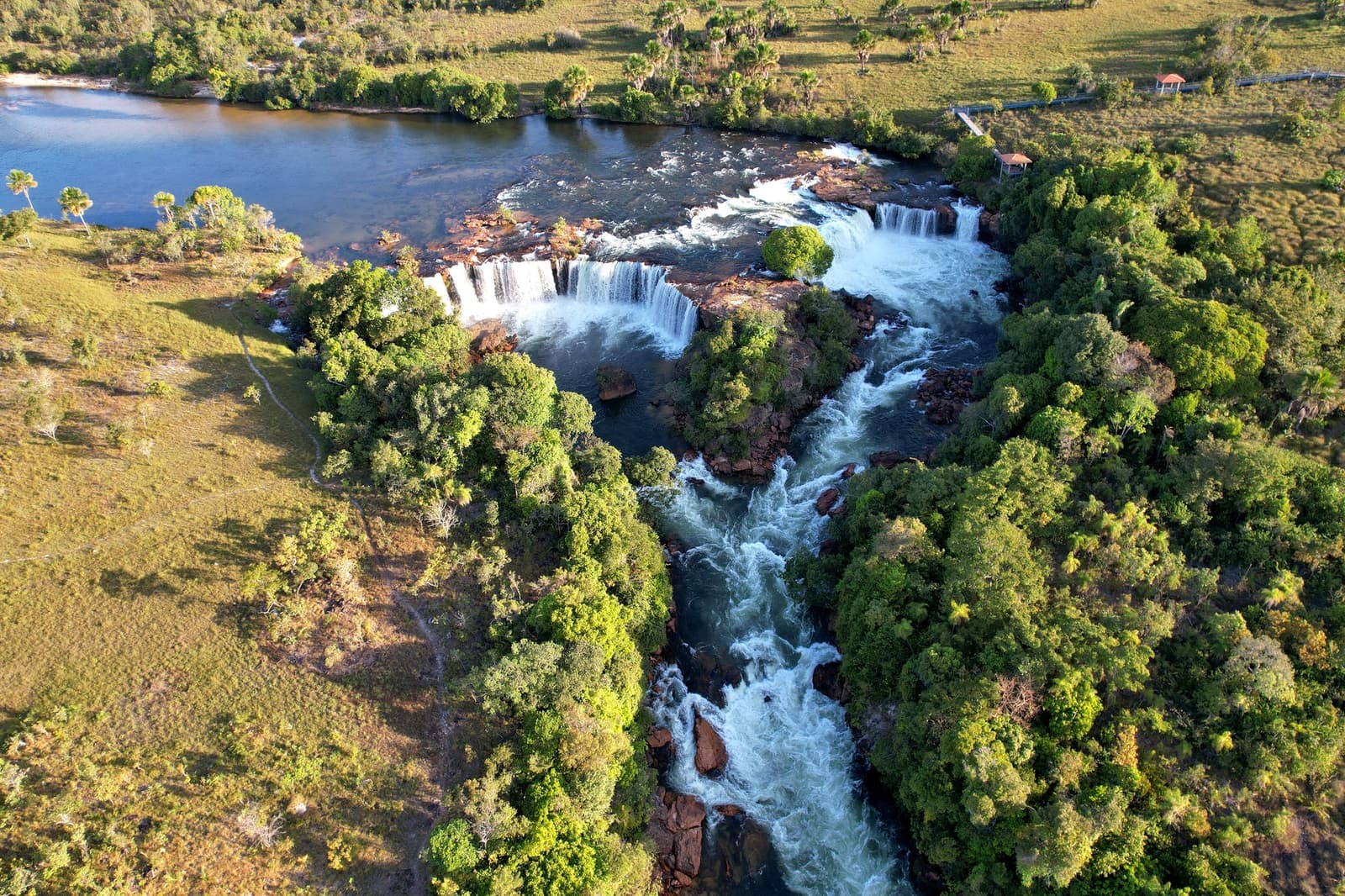 Gravity doing all the work, the river has no interest in slowing down. Photo: Wirestock Aerial view of a wide multi-tiered waterfall on a Jalapão trip, where a river drops over iron-rich rock ledges into a churning gorge flanked by dense Cerrado gallery forest and open grassland