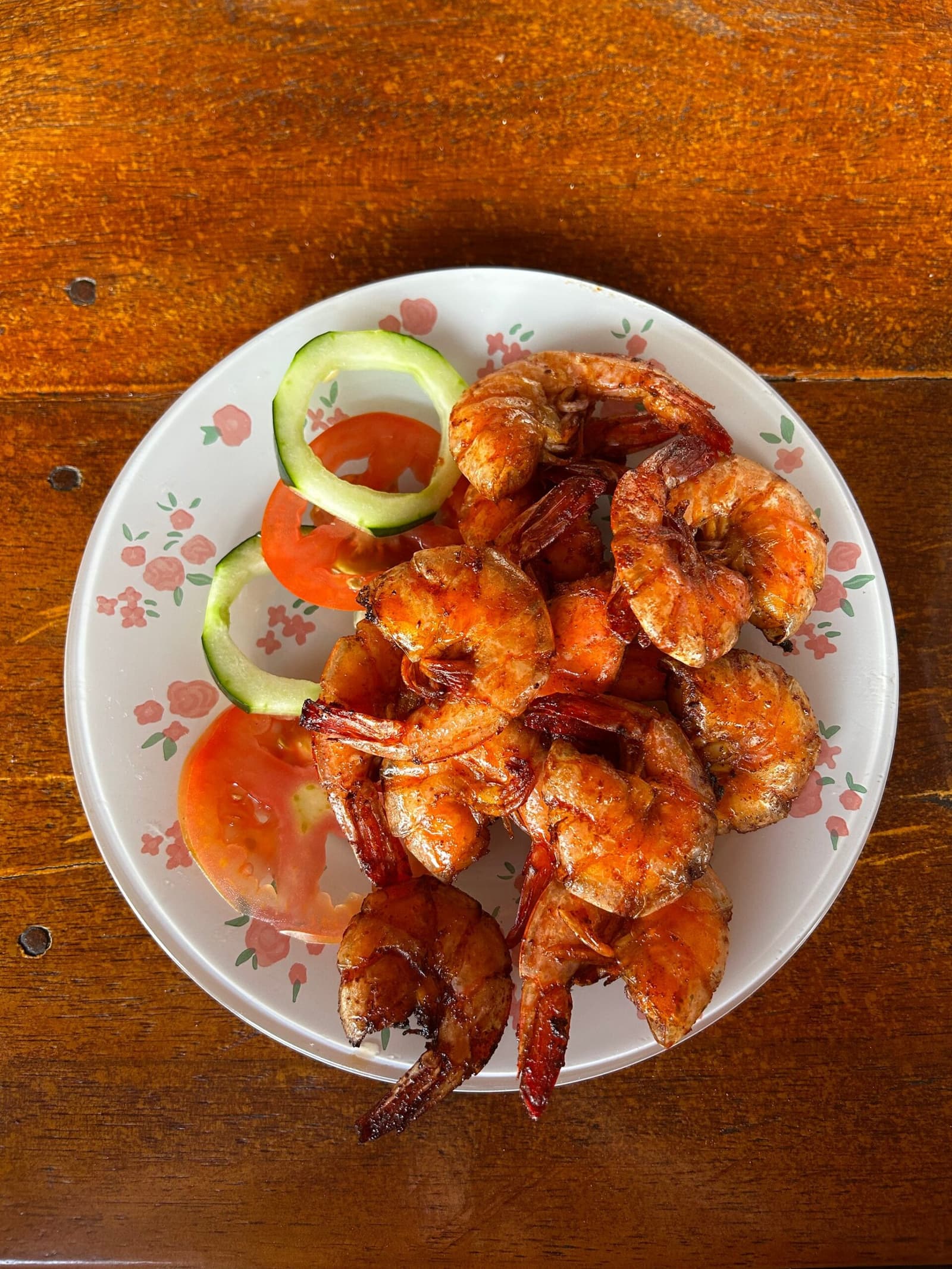 The kind of shrimp plate that makes you cancel your afternoon plans. Overhead view of a plate of grilled whole shrimp with tomato and cucumber slices on a floral-patterned dish, served at a local restaurant near Lençóis Maranhenses Santo Amaro