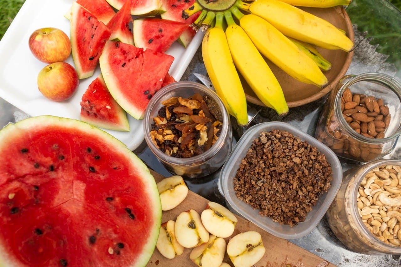Fruit, nuts, granola, the support vehicle earns its keep. Overhead view of a cycling bahia tour snack spread with sliced watermelon, bananas, apples, granola, dried fruit, almonds, and cashews laid out on a tray outdoors
