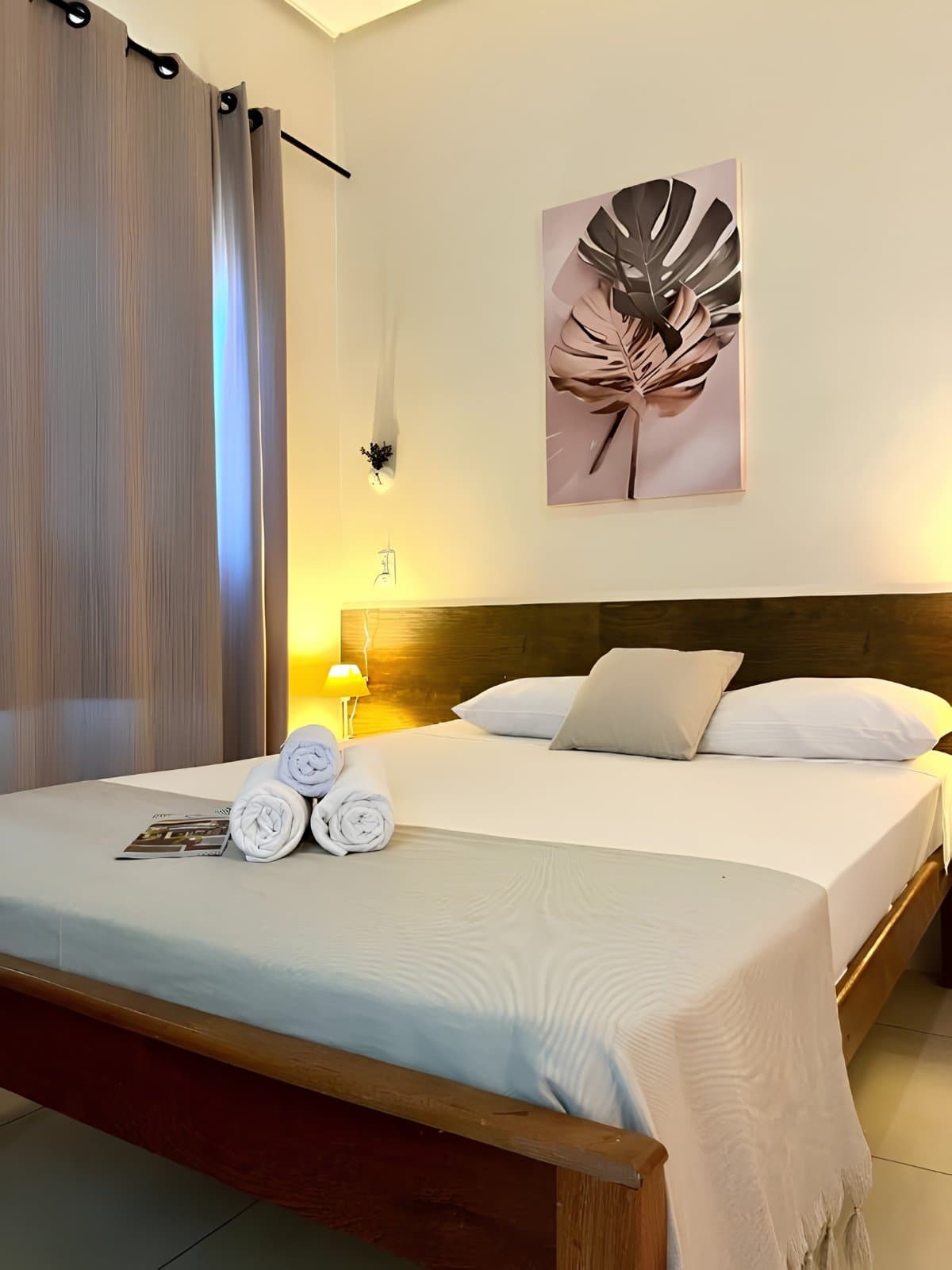Clean sheets, warm lamplight, and a good night's sleep earned on the trail. Neatly made double bed with rolled white towels and a botanical print on the wall in a cozy guesthouse room on a Jalapão adventure