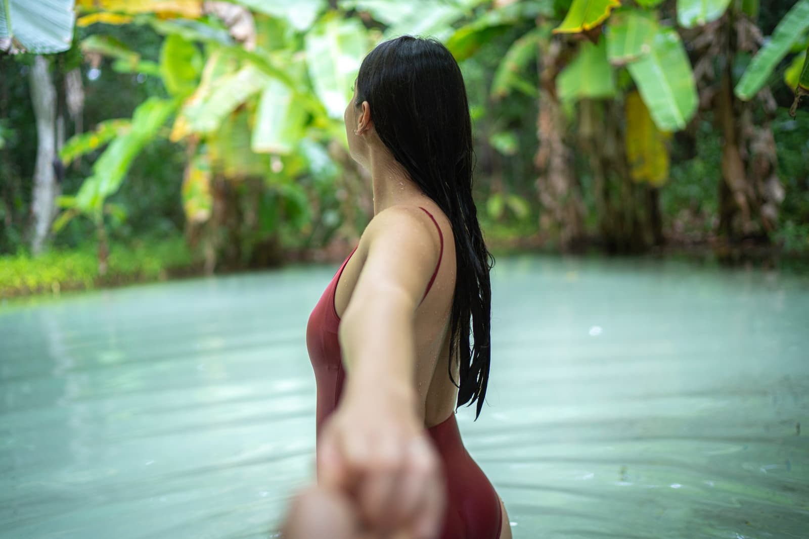 You reach out, the water pulls back. That is a fervedouro for you. Photo: FG Trade A woman in a red swimsuit wading through the calm, pale green waters of a fervedouro on a Jalapão trip, surrounded by lush tropical vegetation including banana trees