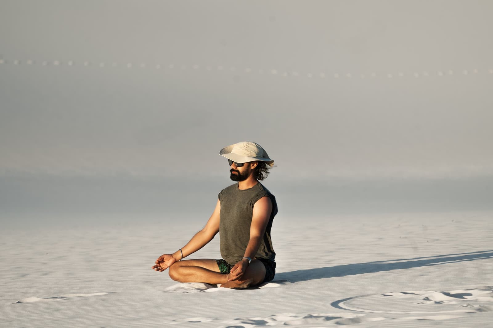 Some places are quiet enough to actually hear yourself think. A bearded man in a cap and sunglasses sits cross-legged in a lotus pose on the vast white sand flats of the Lençóis Maranhenses hike, the hazy horizon stretching far behind him
