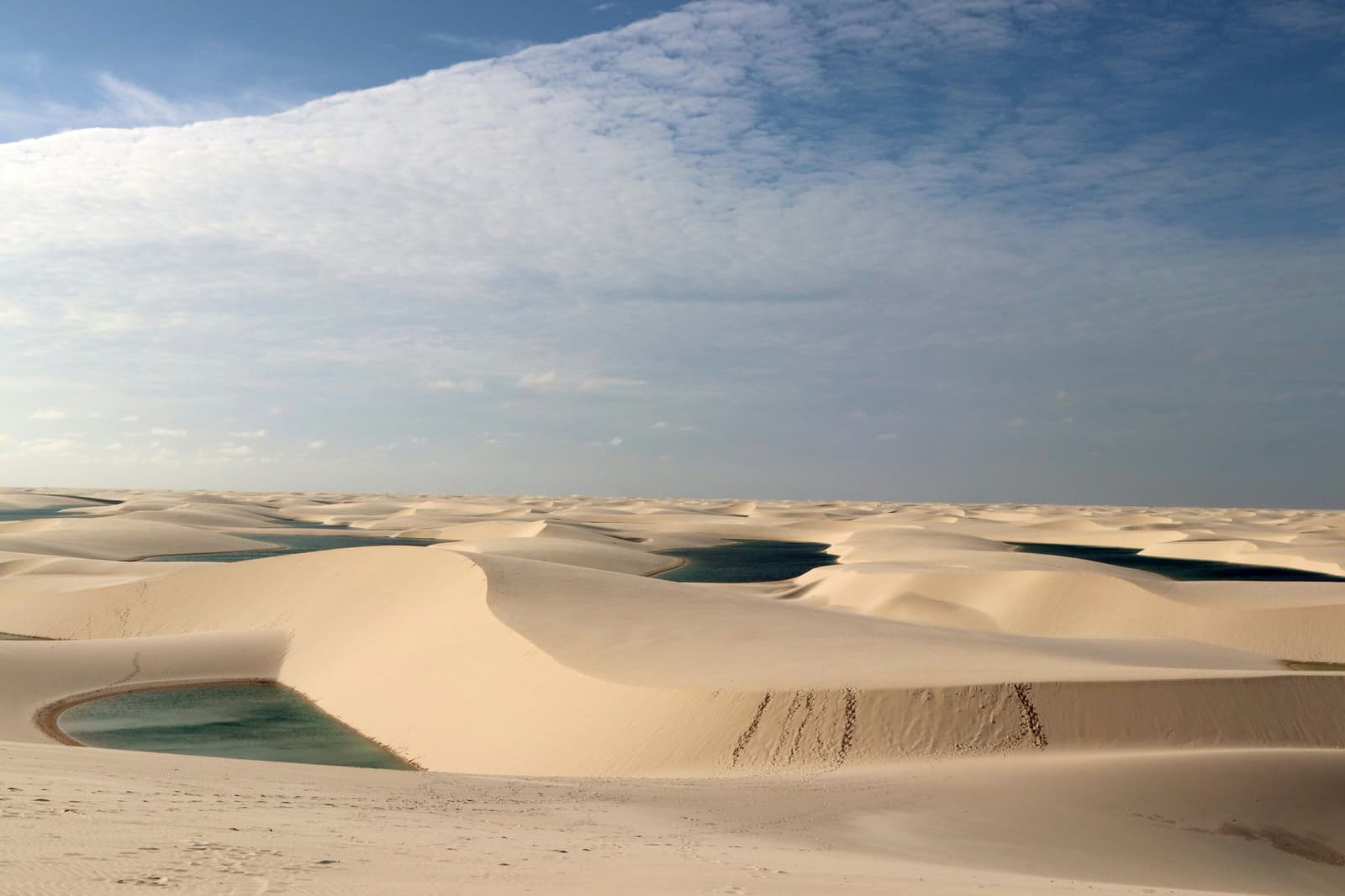 Sand and sky, interrupted only by pools of cool water. Not bad for a national park. Vast white sand dunes of Lençóis Maranhenses Santo Amaro stretch to the horizon, with several turquoise and green rainwater lagoons nestled between the dune ridges under a broad blue sky