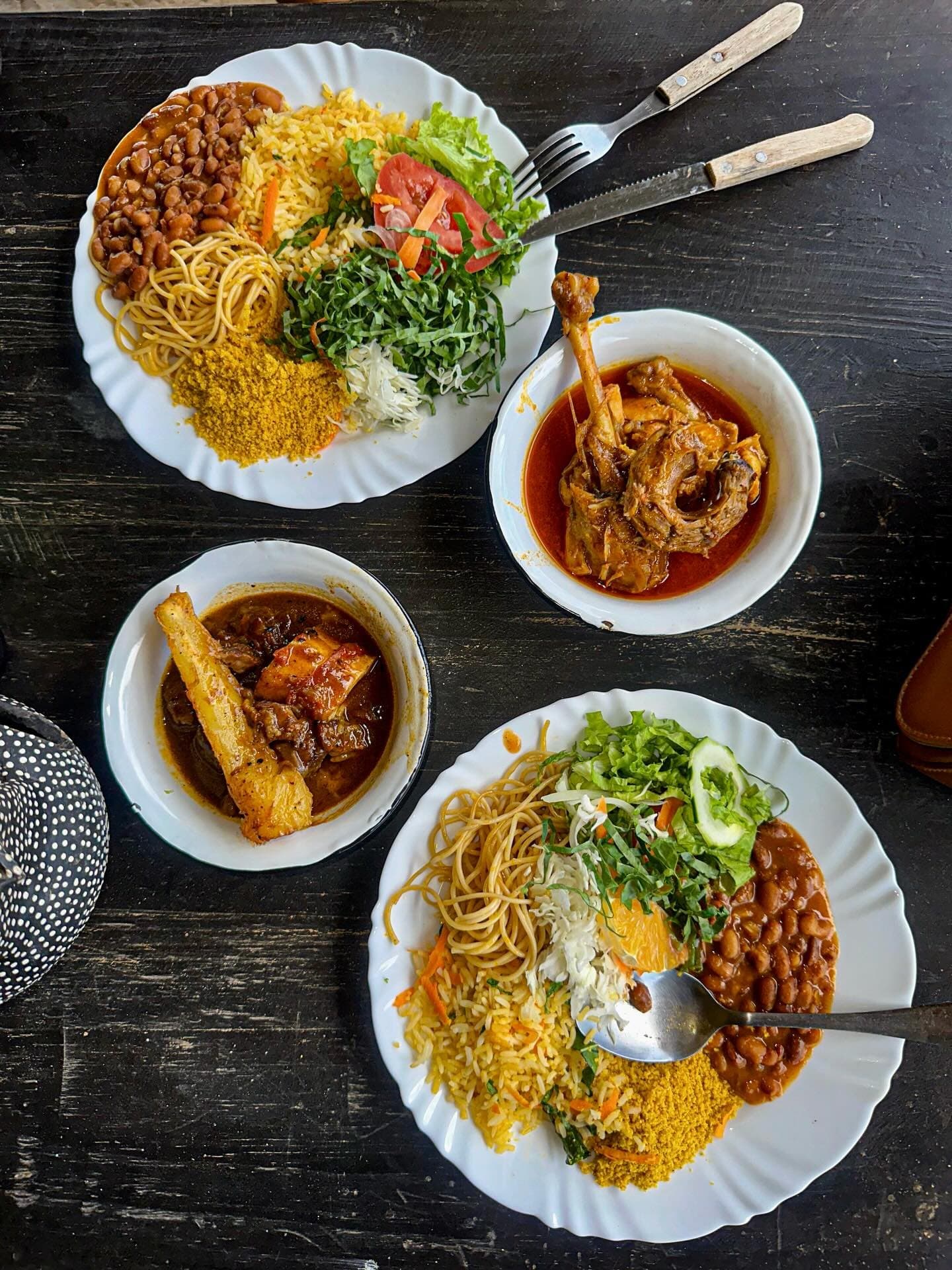 Lunch here is not a side note, it's half the trip. Overhead view of two generous plates of rice, farofa, noodles, beans, and fresh salad alongside two bowls of braised meat in rich sauce, served at a local restaurant near Lençóis Maranhenses Santo Amaro