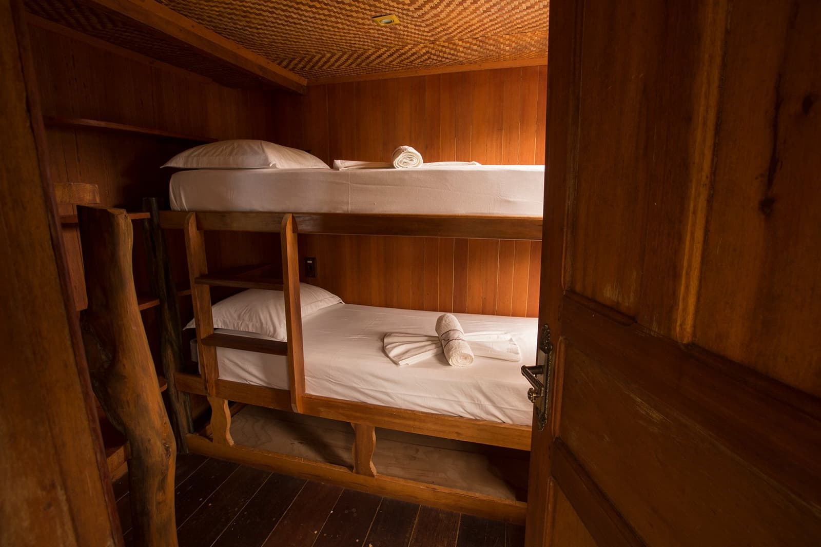 Compact, warm, and clean, river life has its own kind of comfort. Wooden bunk beds with white linen and rolled towels inside a compact Amazon cruise trip in Brazil cabin, with warm timber-panelled walls and a woven ceiling