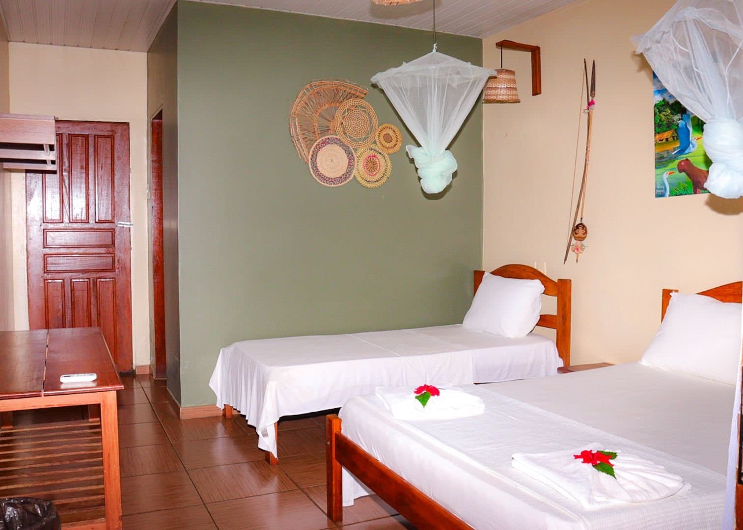 Clean, comfortable, and ready for you after a long day on the river. Twin bedroom at Amazon Turtle Lodge with white linens, hanging mosquito nets, woven basket wall art, and a tropical flower towel fold on the bed