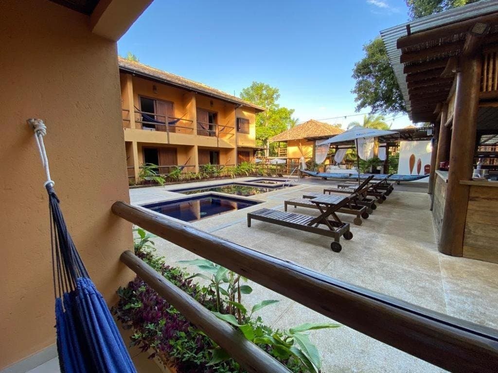 Pool, hammock, and nowhere you need to be until morning. View from a balcony with a blue hammock overlooking the pool, sun loungers, and two-storey guesthouse courtyard on a cycling bahia tour stop in Itacaré
