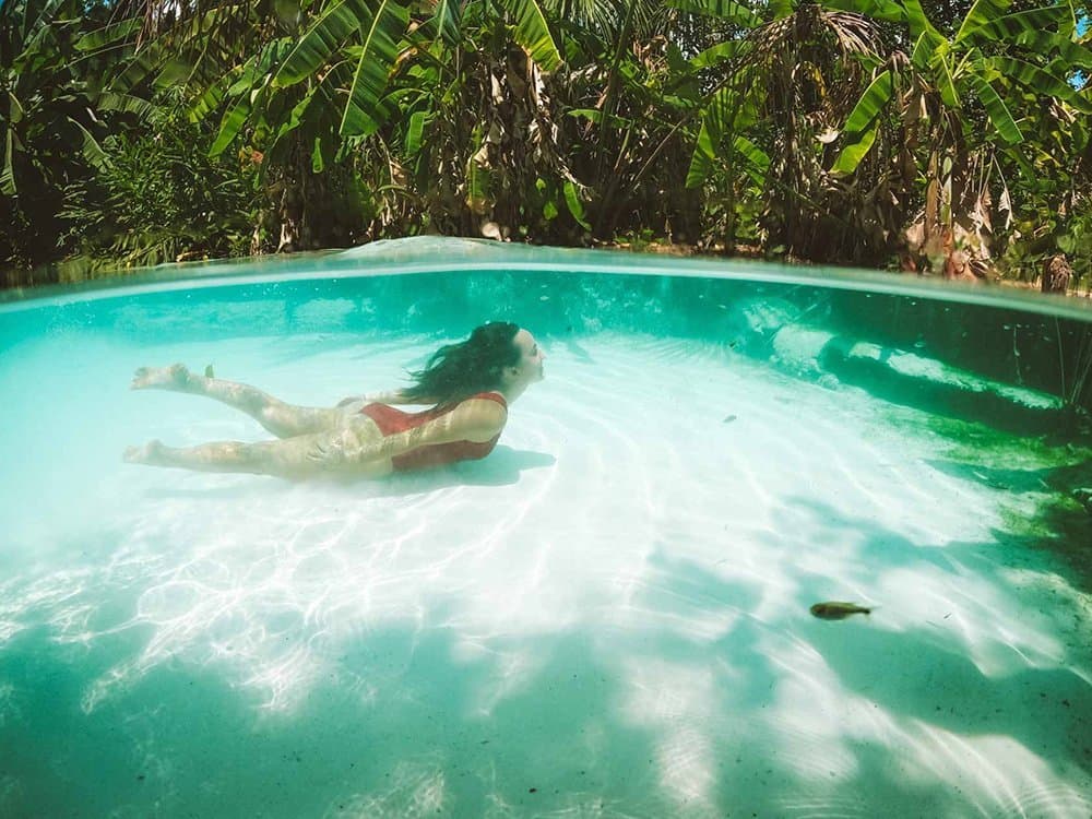 Sink? Not possible. Float? Completely inevitable. Woman in a red bikini floating underwater in the crystal-clear turquoise water of a fervedouro natural spring on a jalapão trip, with a white sandy bottom and lush tropical foliage above the waterline