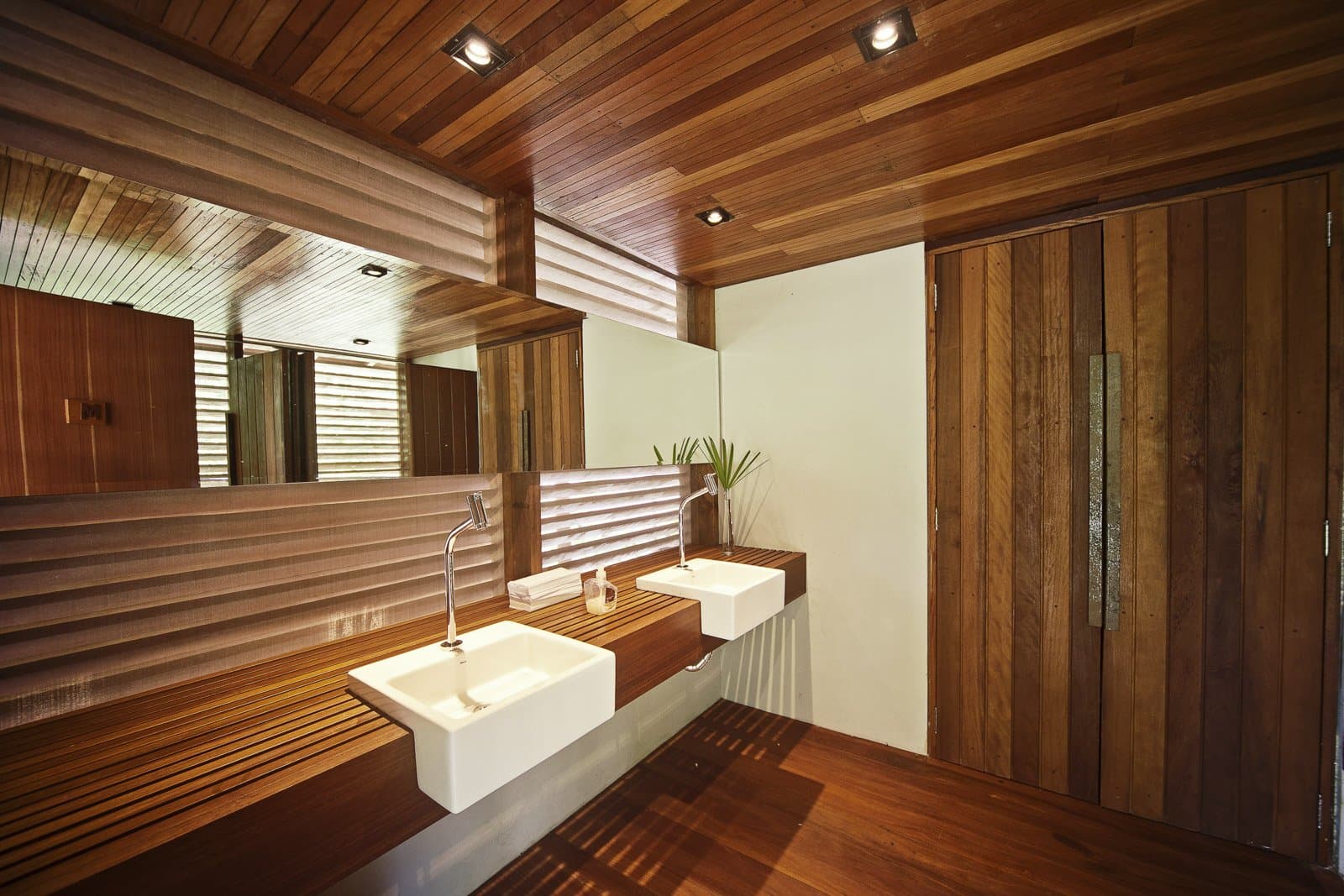 Hot water, warm wood, and no compromises on comfort after a long day in the forest. Photo: Samuel Melim (c) Eco-lodge bathroom with two white vessel sinks on a slatted hardwood vanity, matching wood-panelled walls and ceiling, louvred ventilation windows, and recessed spotlights at a birdwatching in the amazon rainforest lodge