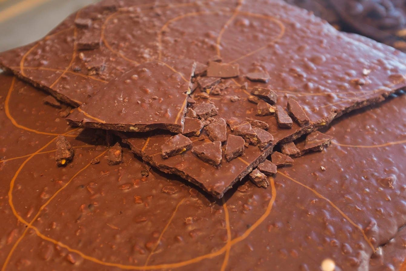 Smash it, taste it, repeat. Fazenda Vila Rosa's chocolate needs no ceremony. Broken shards of handmade chocolate with nut inclusions scattered over a thin chocolate slab on a marble-patterned surface, part of a cocoa farm tasting on the cycling Bahia cocoa route