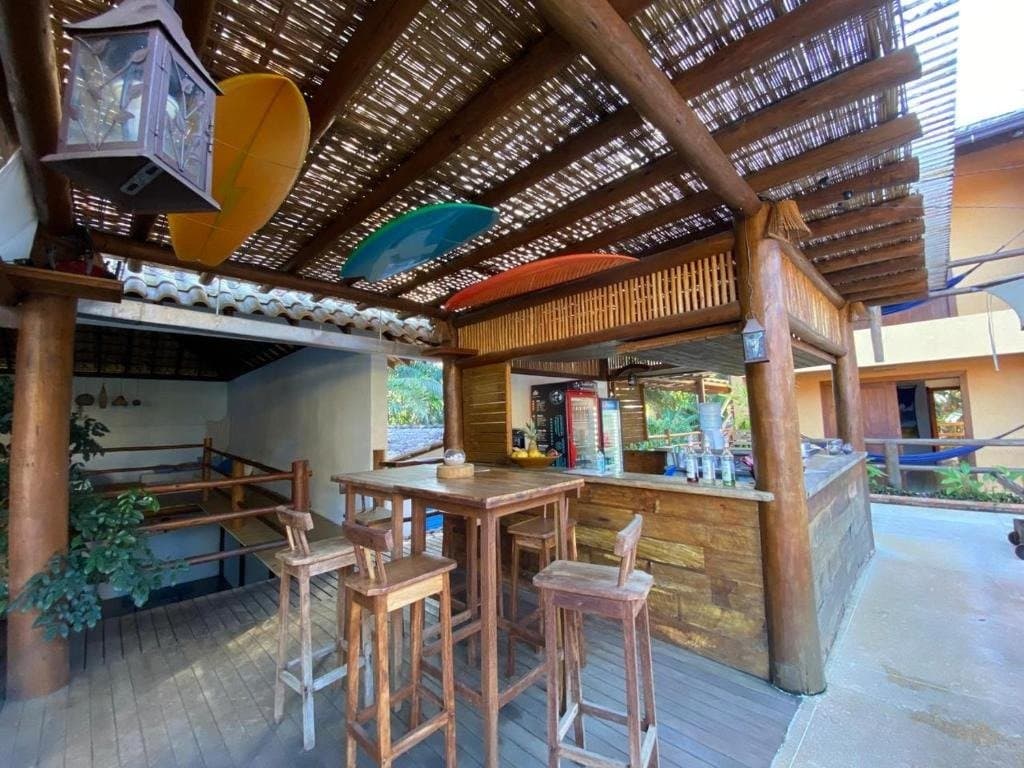 Stools free, drinks cold, kayaks on the ceiling, someone had their priorities right. Open-air wooden bar with log-post pergola, bamboo ceiling, bar stools, and colorful kayaks mounted overhead at a guesthouse on the Bahia cycling route