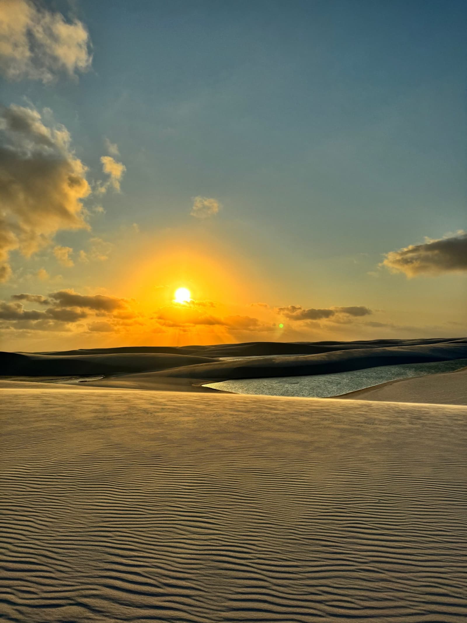 The desert that forgot it was supposed to be dry. Golden sunset over rippled white sand dunes with a shallow lagoon reflecting the light in Lençóis Maranhenses trekking country