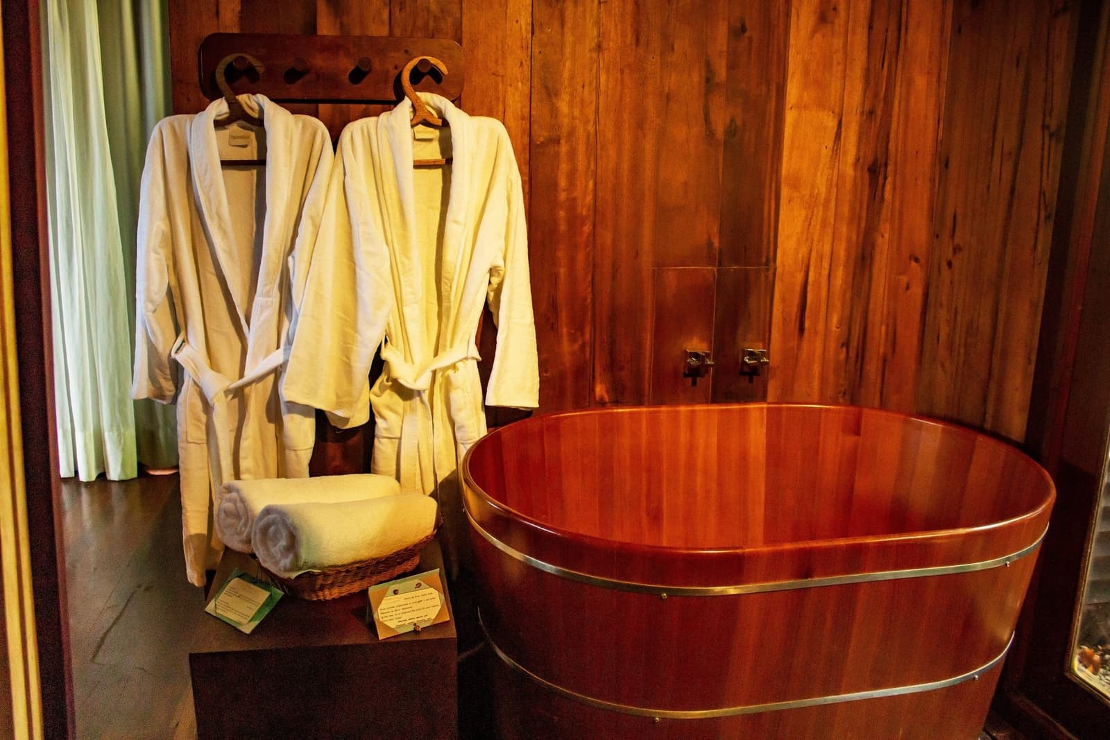 After a day on the river, this is exactly where you want to be. A polished round cedar soaking tub with brass fittings beside two white bathrobes hanging on a wooden rack at Mirante do Gavião, with rolled towels in a wicker basket nearby
