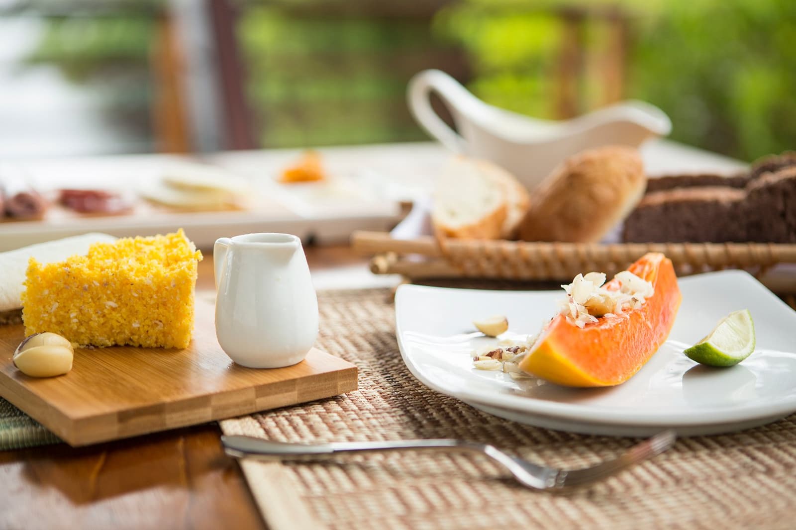 Mornings here start with ripe papaya and local cake, the jungle can wait a few minutes. A fresh papaya wedge topped with nuts and lime alongside a slice of golden cornbread on a bamboo board, served at Mirante do Gavião with a basket of artisan breads in the background