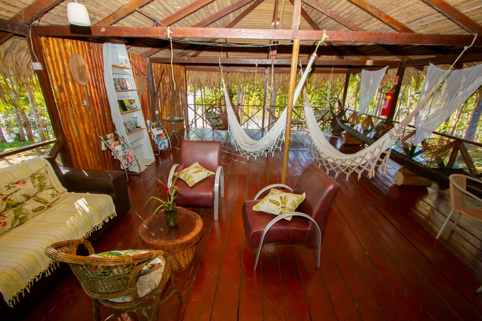 Pick a hammock, grab a book, let the forest do the rest. Open-air common lounge at the Amazon Turtle Lodge featuring woven hammocks, leather armchairs, rattan furniture, and a polished hardwood deck surrounded by rainforest greenery