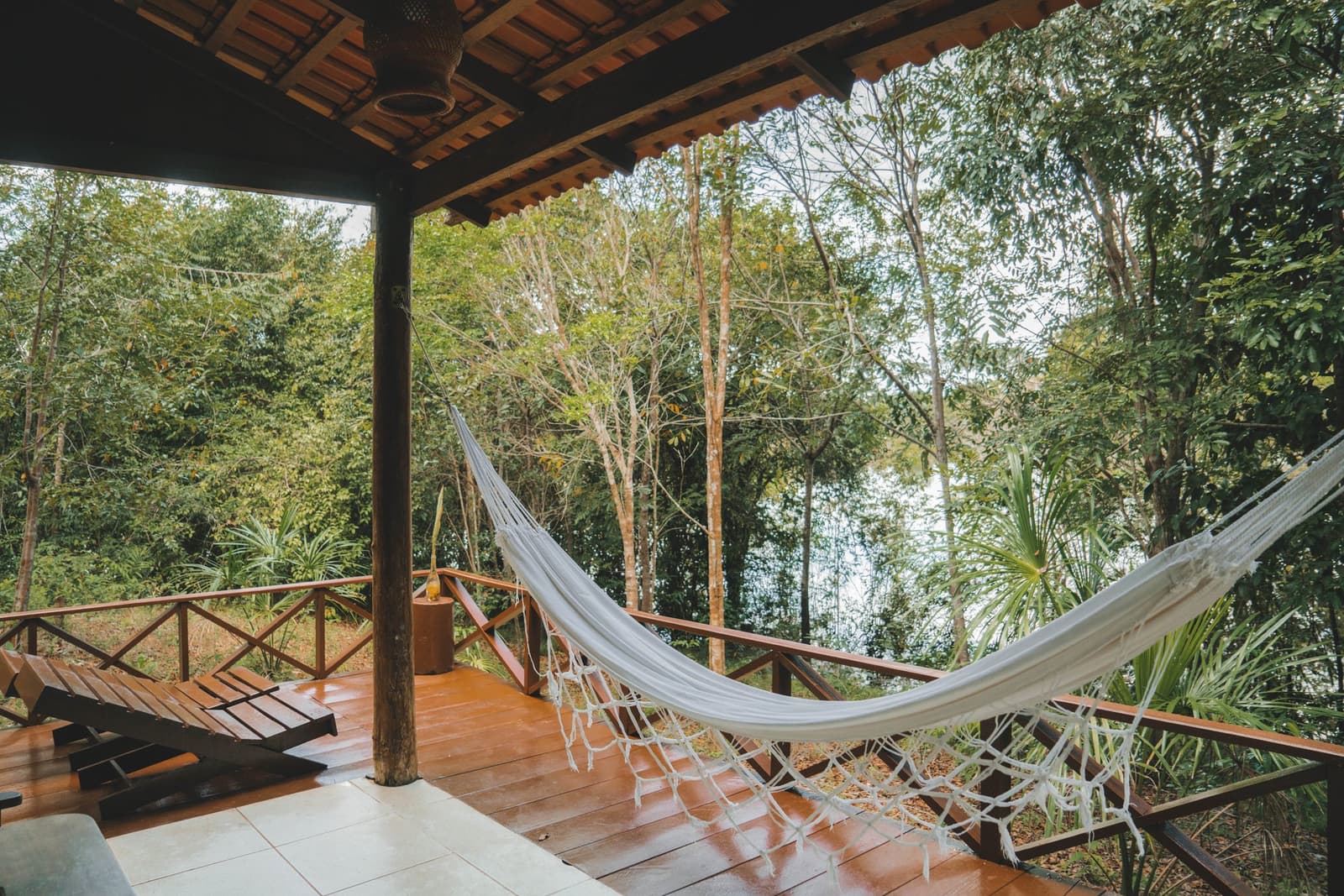 Your afternoon plans, sorted: hammock, canopy, nothing urgent. A white rope hammock hangs on a hardwood deck at the Amazon Turtle Lodge, with a wooden sun lounger and lush green rainforest canopy visible beyond the railing